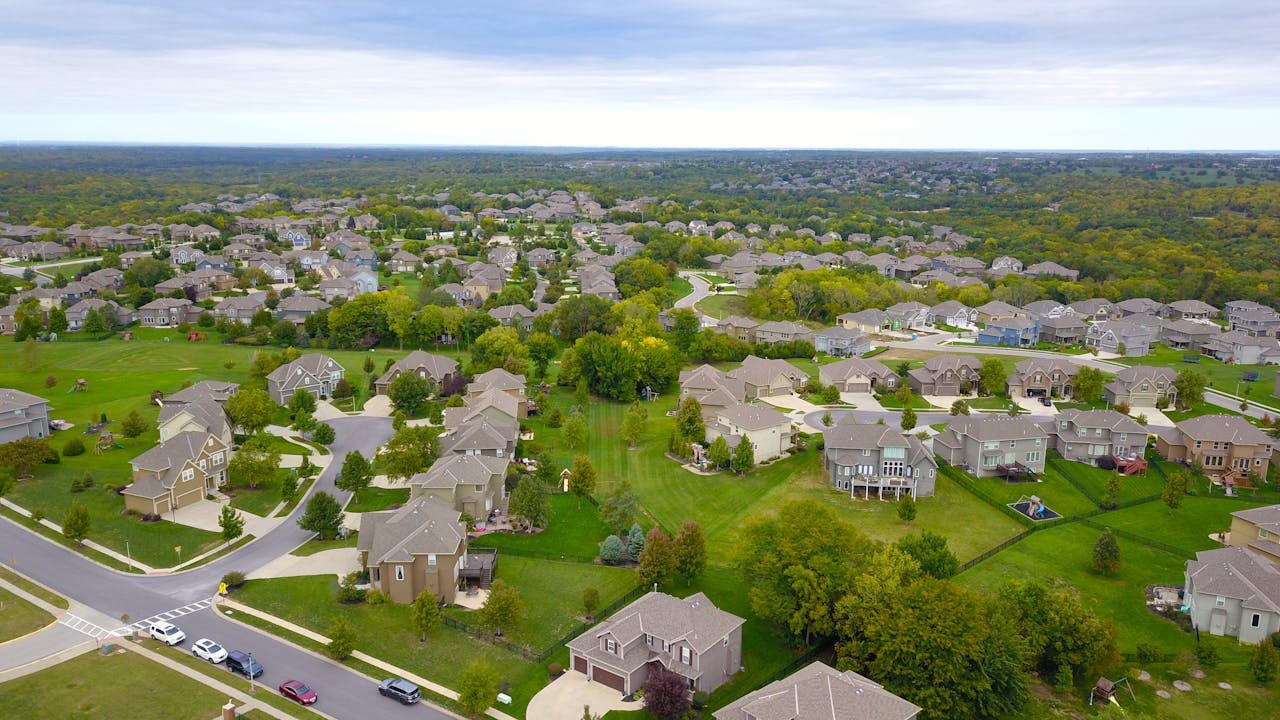 gallery-img-02 Aerial view of a suburban neighborhood with houses, roads, and lush greenery.