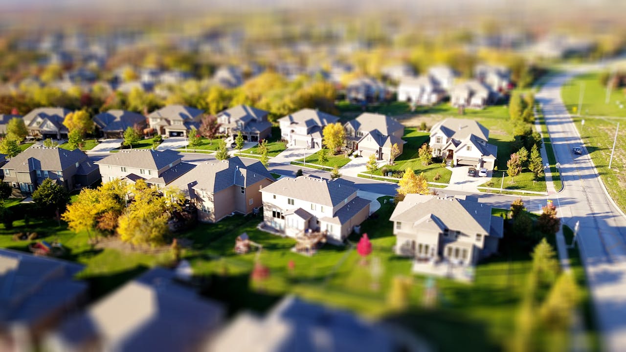 hero-gallery-01 Tilt-shift aerial photo of a suburban neighborhood with green lawns and roads.