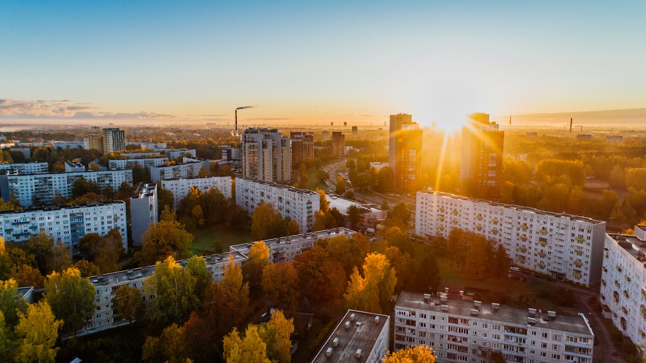 cta-01 Aerial view of a cityscape at sunrise with autumn foliage and modern buildings.
